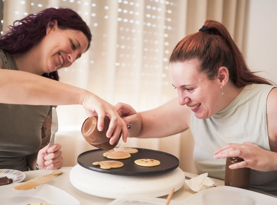 carer helping down syndrome disabled women in cooking pancakes