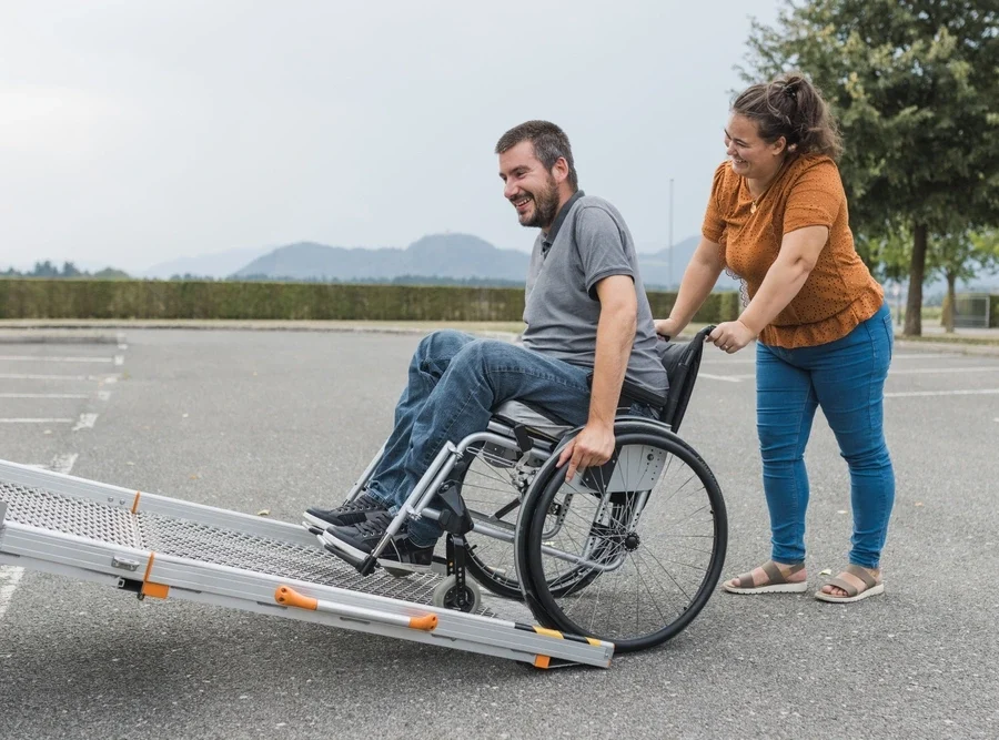 women pushing wheelchair for a disabled man up the van
