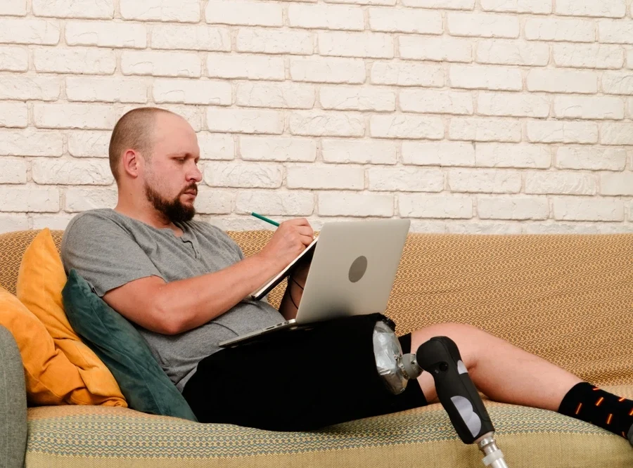 disabled man with a prosthetic leg sitting on sofa and working on laptop